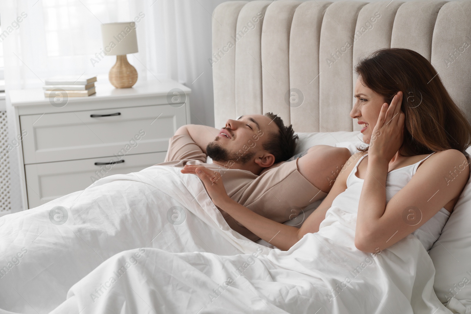 Photo of Bedtime. Irritated woman near her snoring husband in bed at home