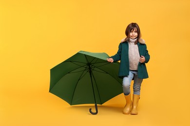 Cute little girl with green umbrella on yellow background