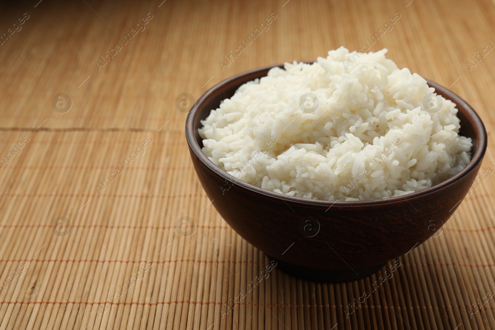 Photo of Tasty cooked rice in bowl on bamboo mat. Space for text