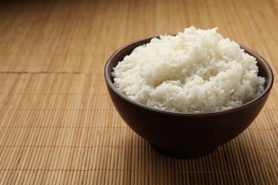 Photo of Tasty cooked rice in bowl on bamboo mat. Space for text