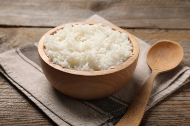 Photo of Tasty cooked rice in bowl and spoon on wooden table