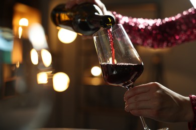 Woman pouring red wine from bottle into glass on blurred background, closeup