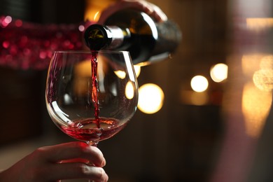 Woman pouring red wine from bottle into glass on blurred background, closeup. Space for text