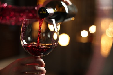 Photo of Woman pouring red wine from bottle into glass on blurred background, closeup. Space for text