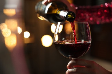 Woman pouring red wine from bottle into glass on blurred background, closeup. Space for text
