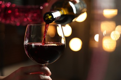 Woman pouring red wine from bottle into glass on blurred background, closeup. Space for text