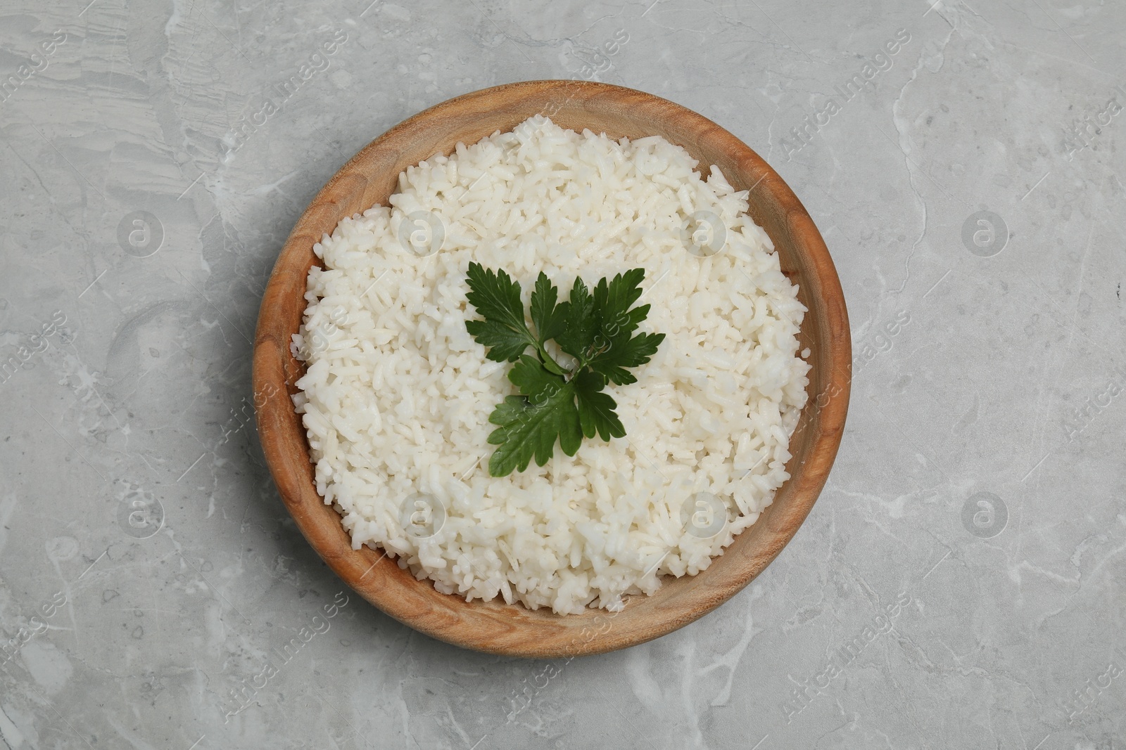 Photo of Tasty cooked rice with parsley in bowl on grey marble table, top view