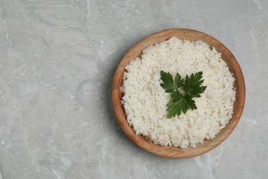 Photo of Tasty cooked rice with parsley in bowl on grey marble table, top view. Space for text