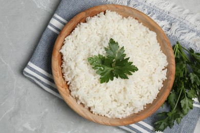 Photo of Tasty cooked rice in bowl with parsley on grey marble table, flat lay