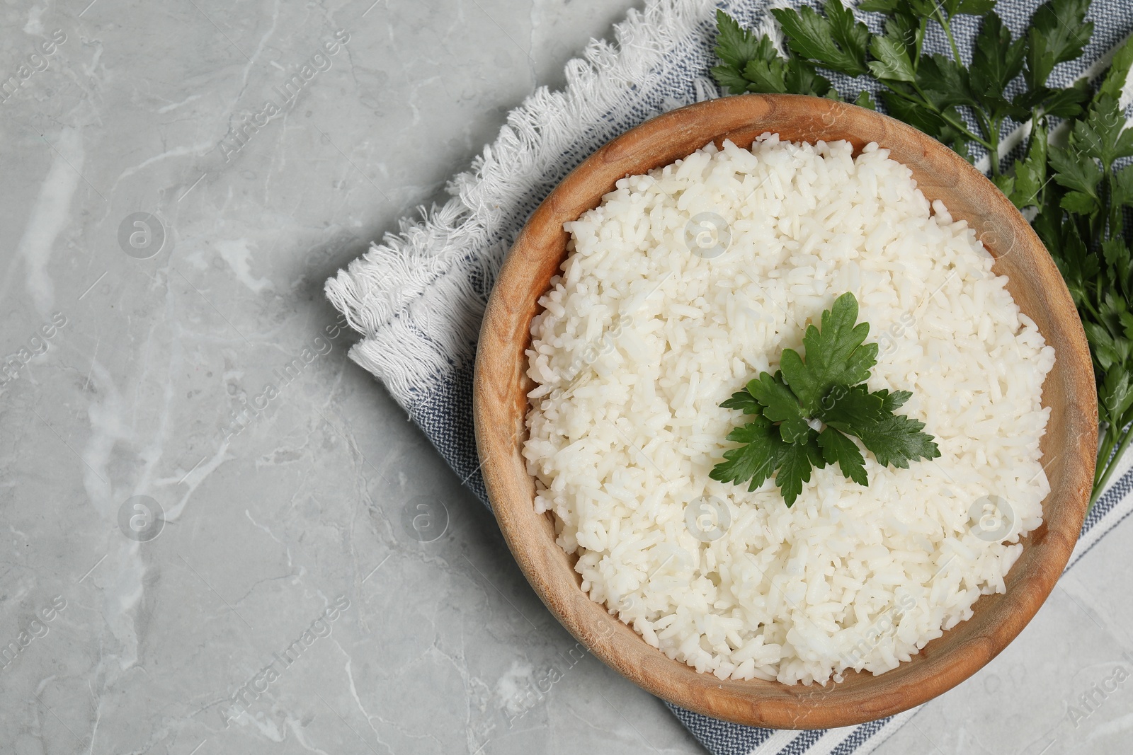 Photo of Tasty cooked rice in bowl with parsley on grey marble table, flat lay. Space for text