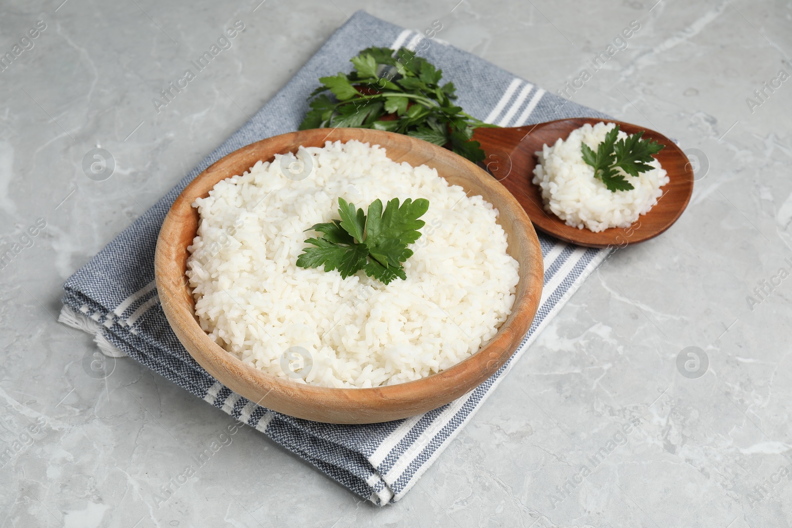 Photo of Tasty cooked rice in bowl with parsley and spoon on grey marble table