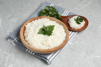 Photo of Tasty cooked rice in bowl with parsley and spoon on grey marble table