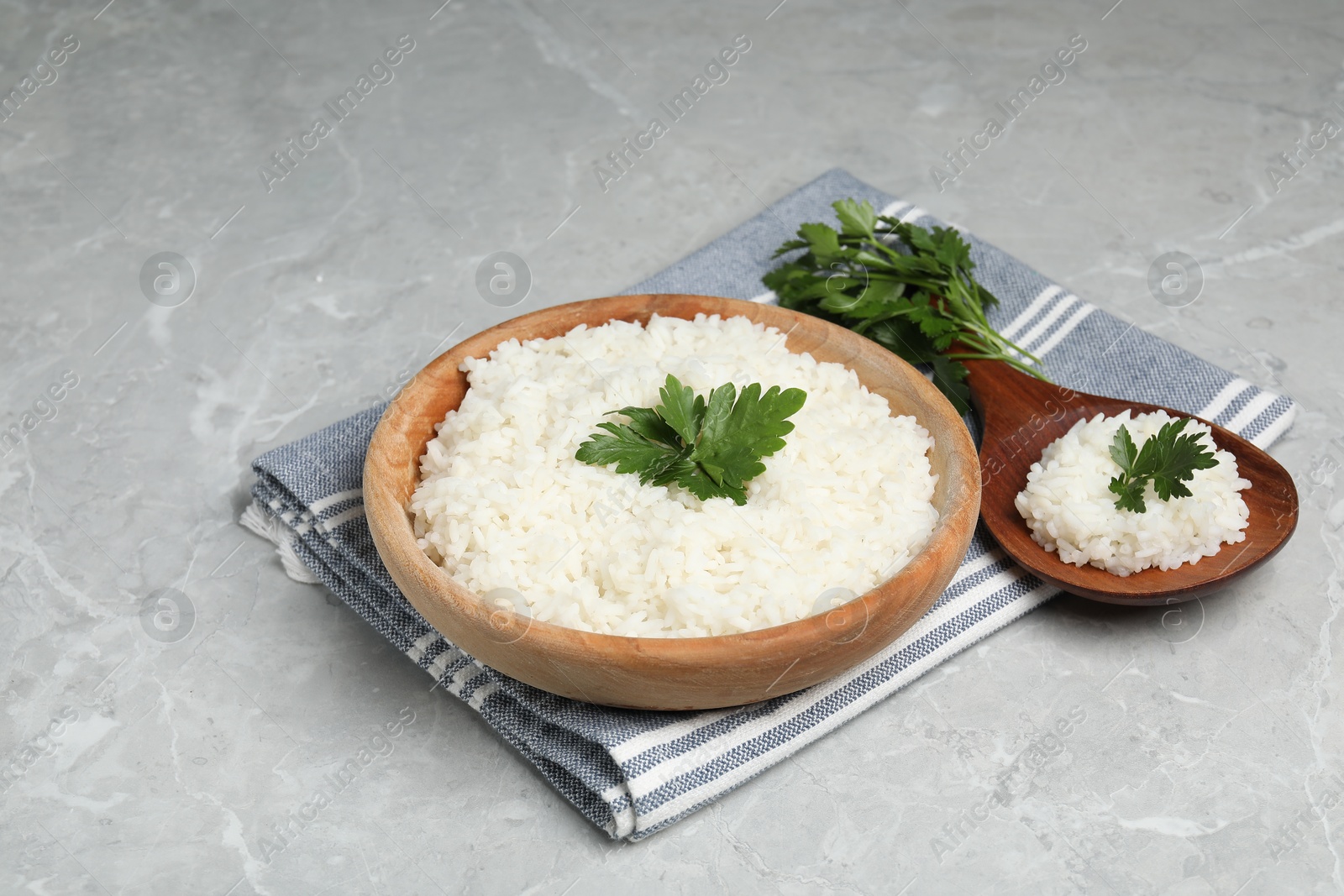 Photo of Tasty cooked rice in bowl with parsley and spoon on grey marble table