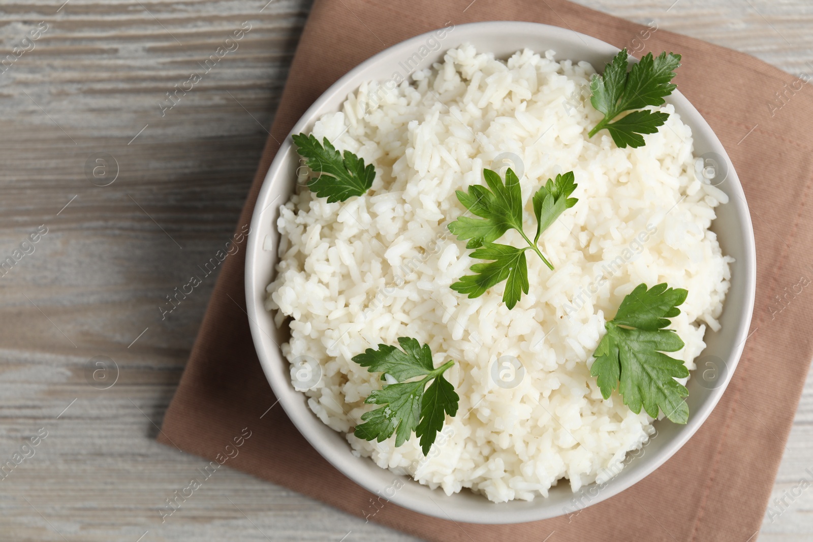 Photo of Tasty cooked rice with parsley in bowl on wooden table, top view