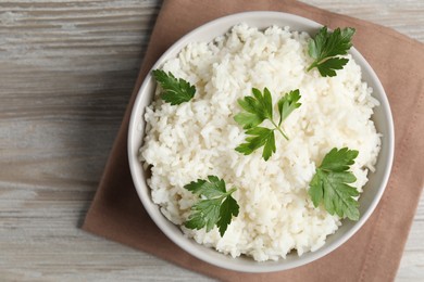 Tasty cooked rice with parsley in bowl on wooden table, top view