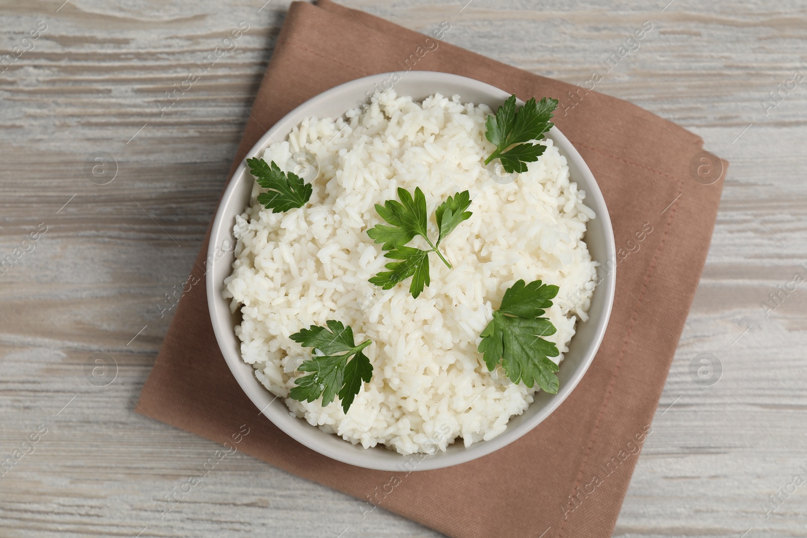 Photo of Tasty cooked rice with parsley in bowl on wooden table, top view