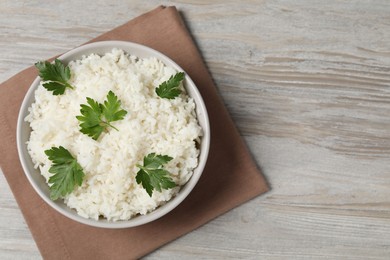 Photo of Tasty cooked rice with parsley in bowl on wooden table, top view. Space for text