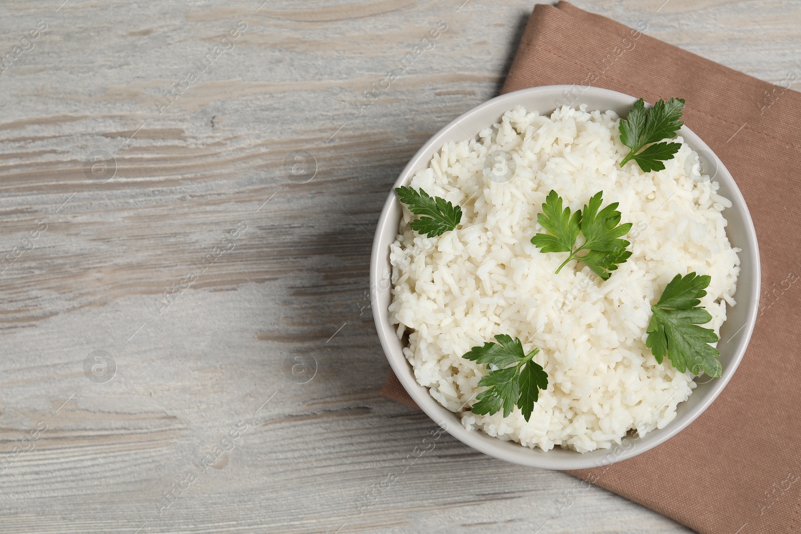 Photo of Tasty cooked rice with parsley in bowl on wooden table, top view. Space for text