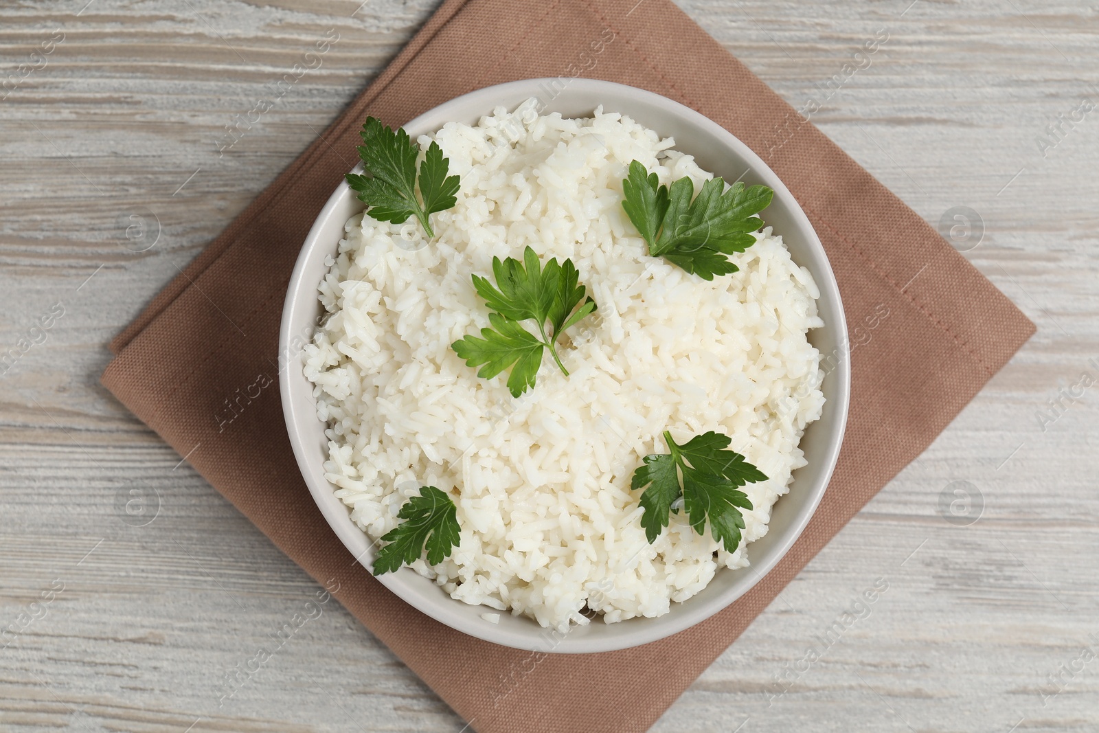 Photo of Tasty cooked rice with parsley in bowl on wooden table, top view