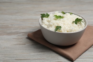 Photo of Tasty cooked rice with parsley in bowl on wooden table. Space for text