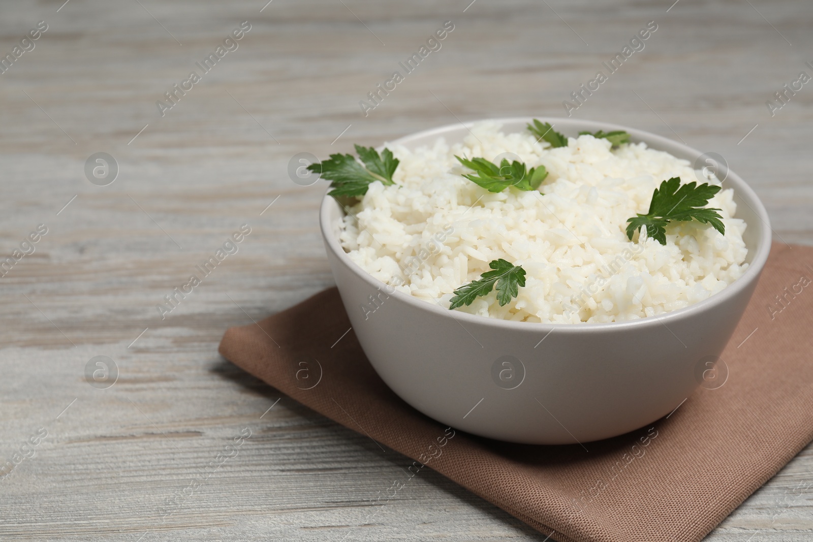 Photo of Tasty cooked rice with parsley in bowl on wooden table. Space for text