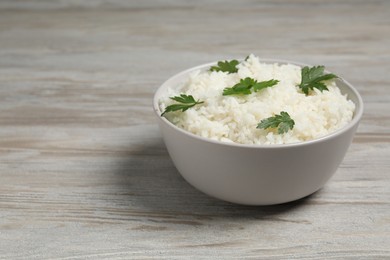 Photo of Tasty cooked rice with parsley in bowl on wooden table. Space for text