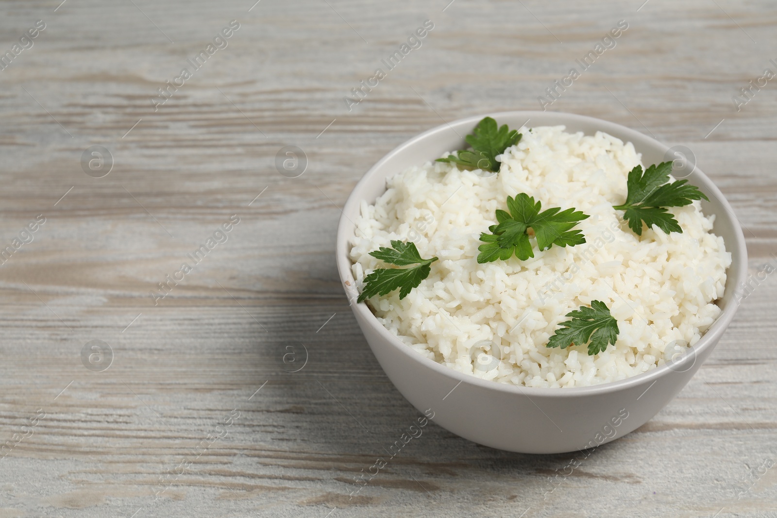 Photo of Tasty cooked rice with parsley in bowl on wooden table. Space for text