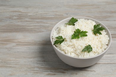 Photo of Tasty cooked rice with parsley in bowl on wooden table. Space for text