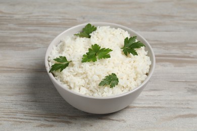 Photo of Tasty cooked rice with parsley in bowl on wooden table