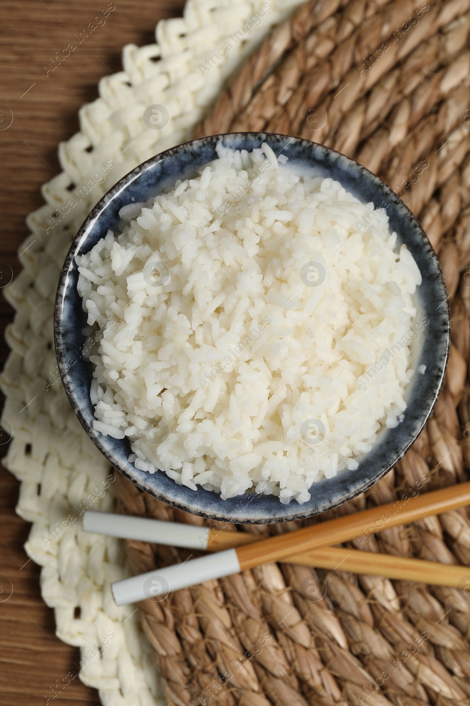 Photo of Tasty cooked rice in bowl and chopsticks on wooden table, flat lay