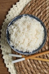 Tasty cooked rice in bowl and chopsticks on wooden table, flat lay