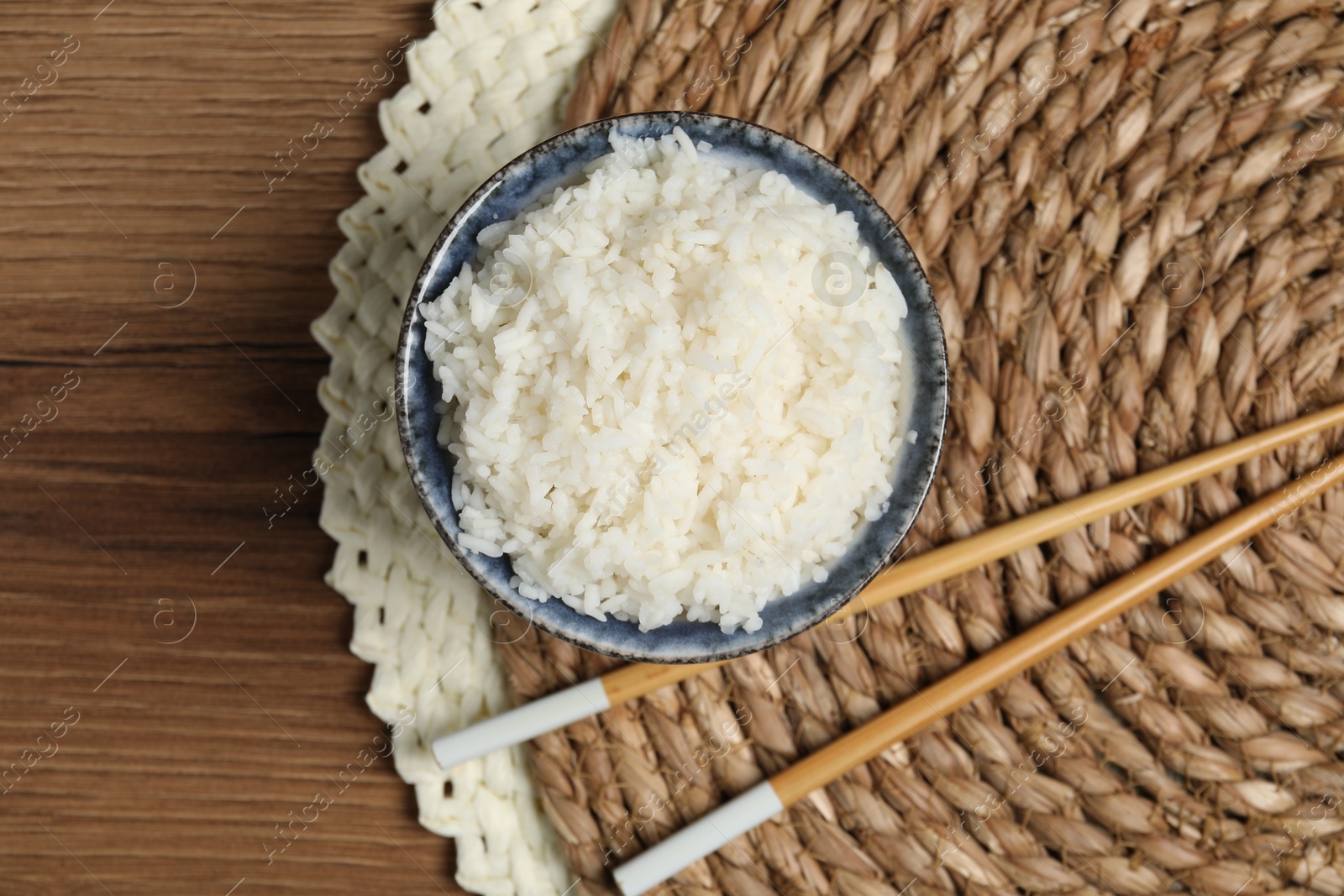 Photo of Tasty cooked rice in bowl and chopsticks on wooden table, flat lay