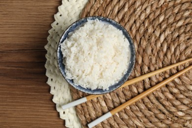 Tasty cooked rice in bowl and chopsticks on wooden table, flat lay