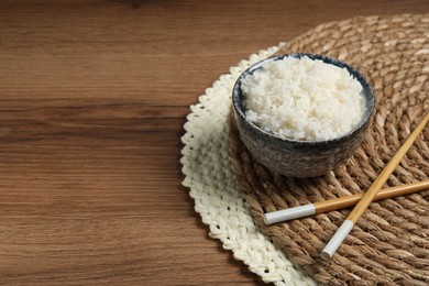 Photo of Tasty cooked rice in bowl and chopsticks on wooden table, space for text