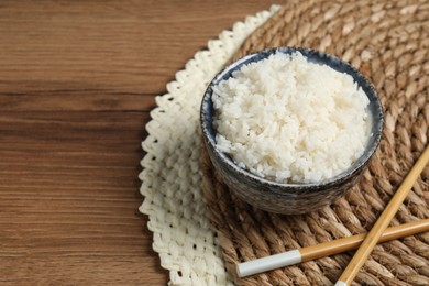 Photo of Tasty cooked rice in bowl and chopsticks on wooden table, space for text