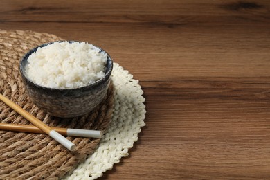 Tasty cooked rice in bowl and chopsticks on wooden table, space for text