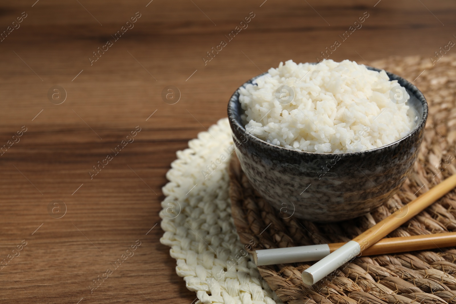 Photo of Tasty cooked rice in bowl and chopsticks on wooden table, space for text