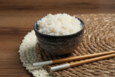 Photo of Tasty cooked rice in bowl and chopsticks on wooden table