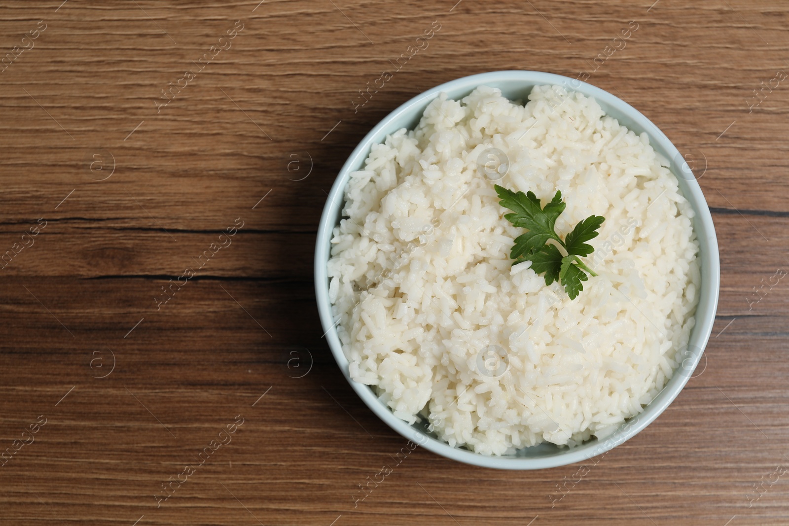 Photo of Tasty cooked rice with parsley in bowl on wooden table, top view. Space for text