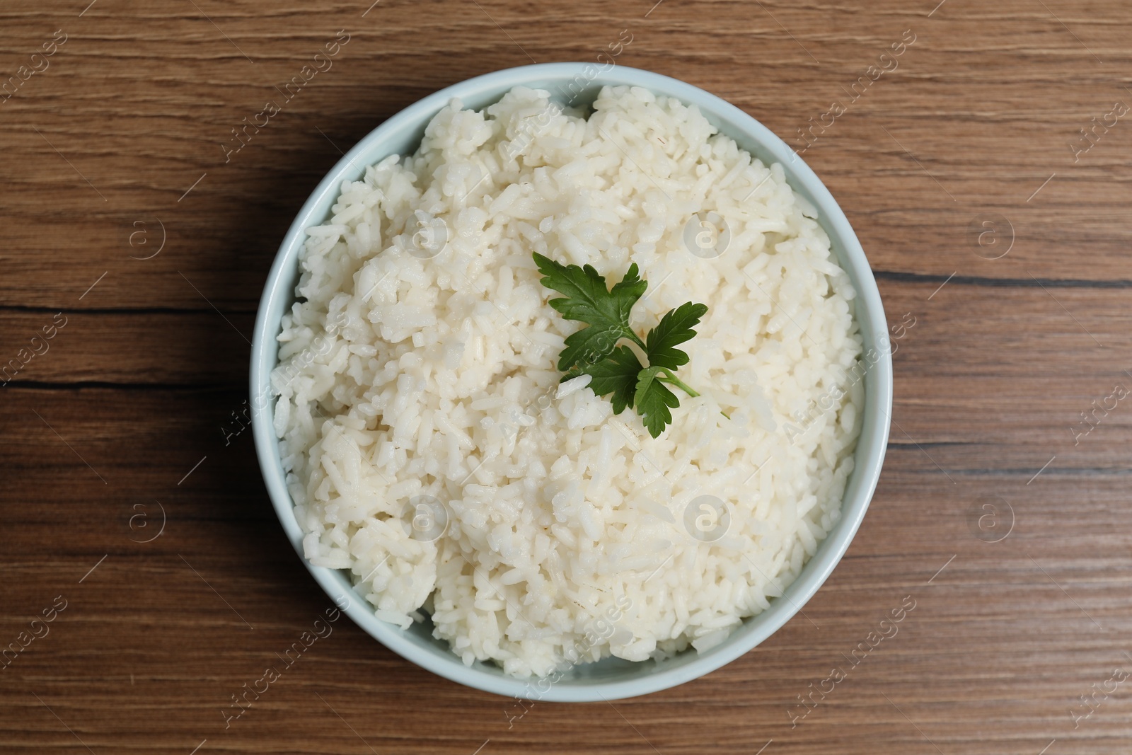 Photo of Tasty cooked rice with parsley in bowl on wooden table, top view