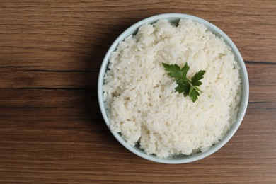 Tasty cooked rice with parsley in bowl on wooden table, top view. Space for text