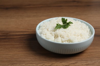 Photo of Tasty cooked rice with parsley in bowl on wooden table. Space for text