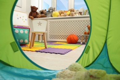 Stylish child room interior with different toys and furniture, view from play tent