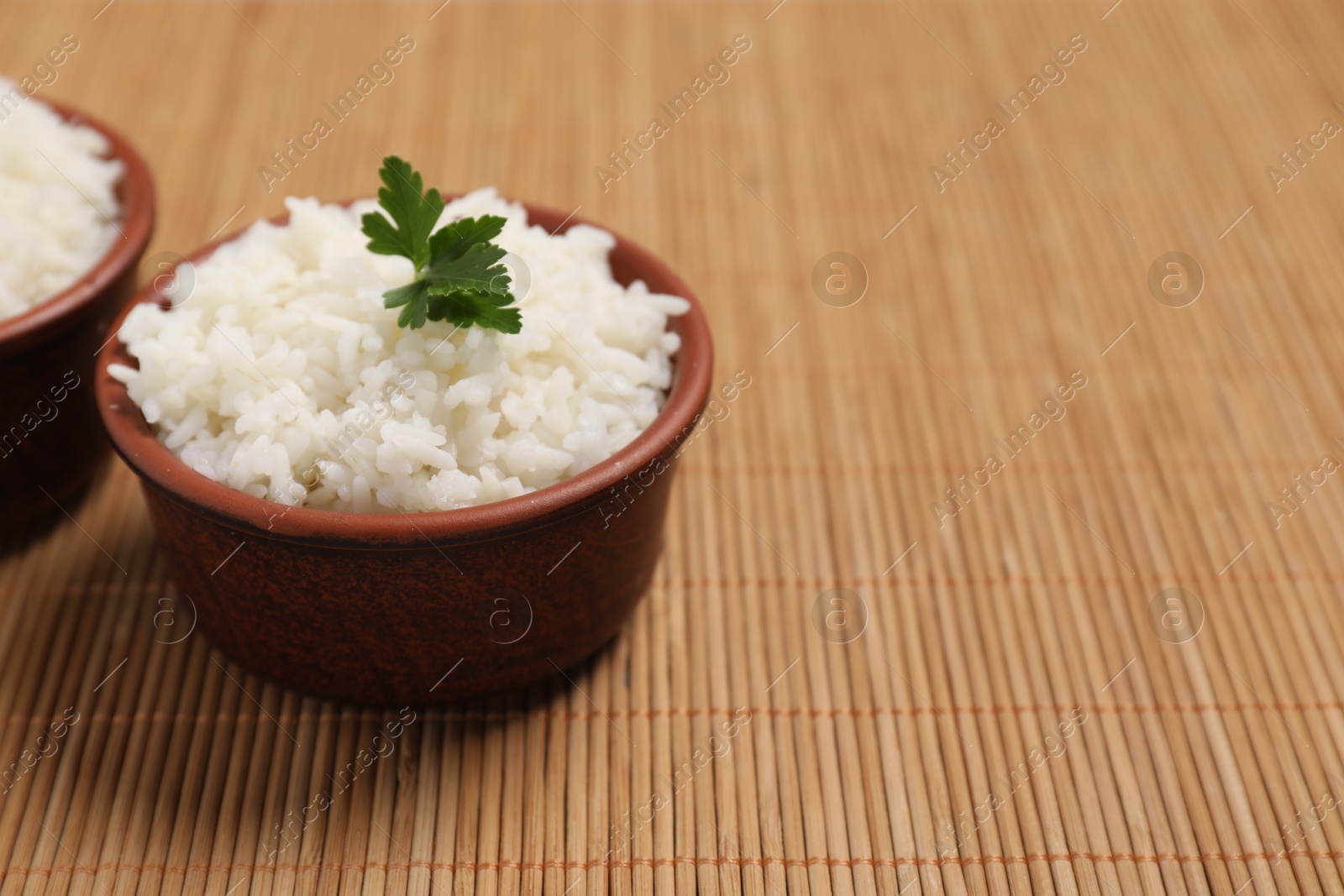 Photo of Bowls of delicious boiled rice with parsley on bamboo mat. Space for text