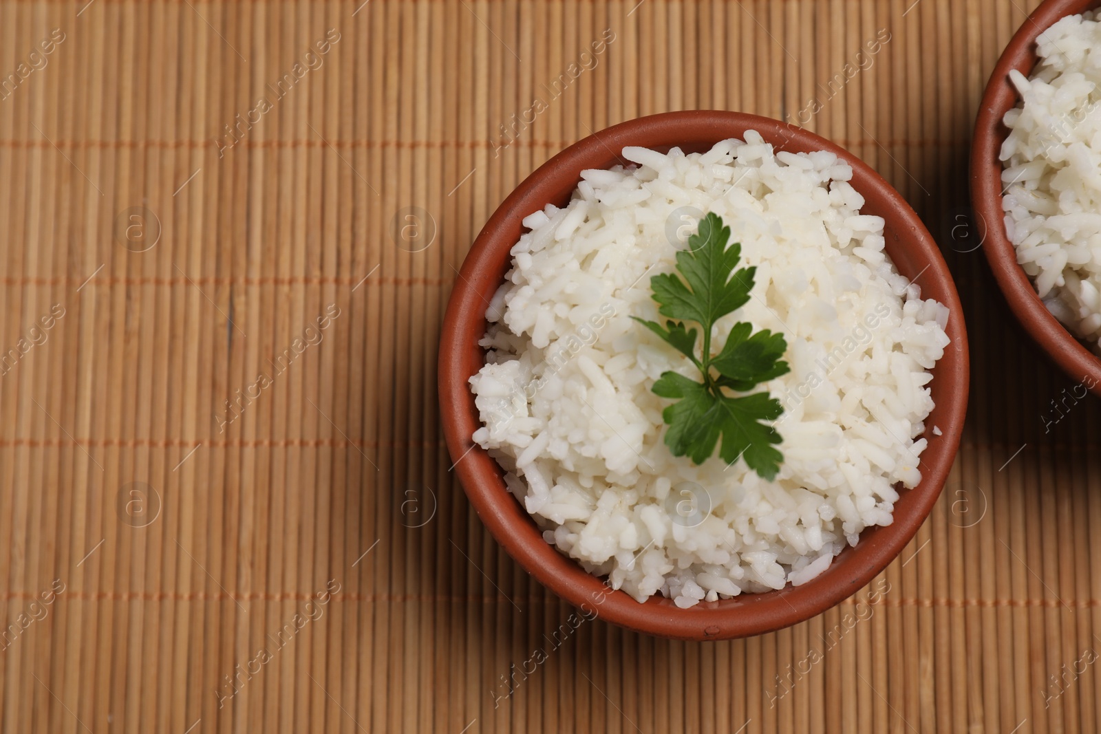 Photo of Bowls of delicious boiled rice with parsley on bamboo mat, top view. Space for text