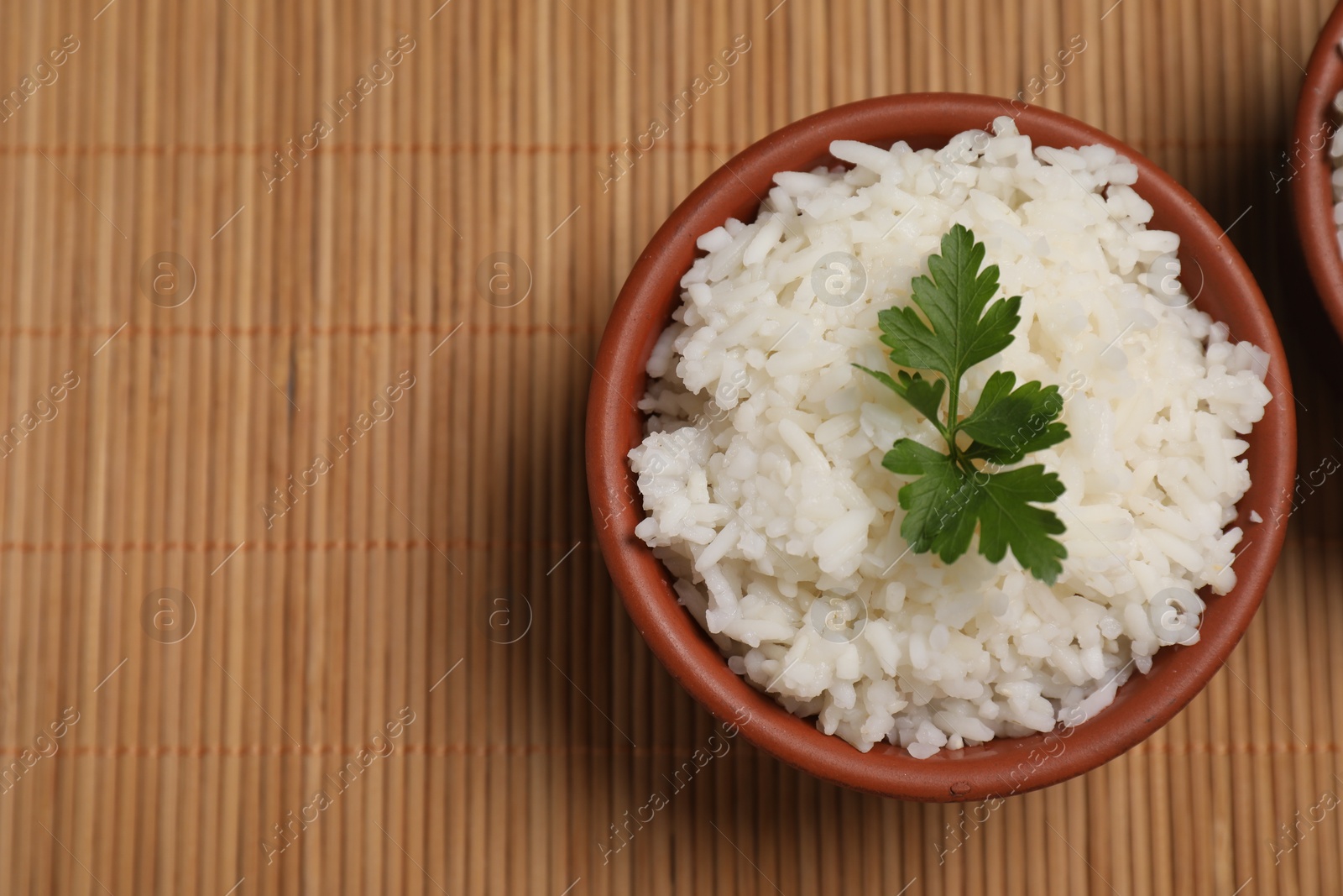 Photo of Bowls of delicious boiled rice with parsley on bamboo mat, top view. Space for text