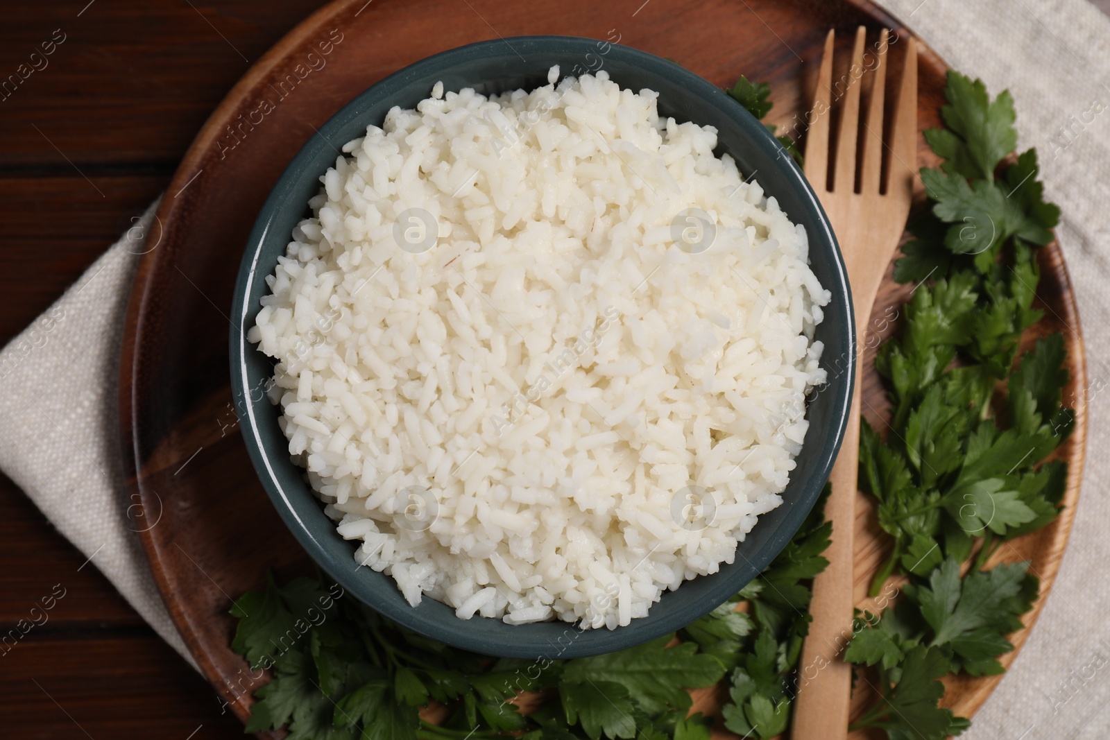 Photo of Delicious boiled rice served with parsley on wooden table, top view