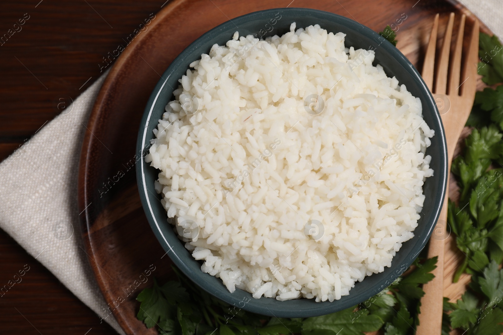 Photo of Delicious boiled rice served with parsley on wooden table, top view