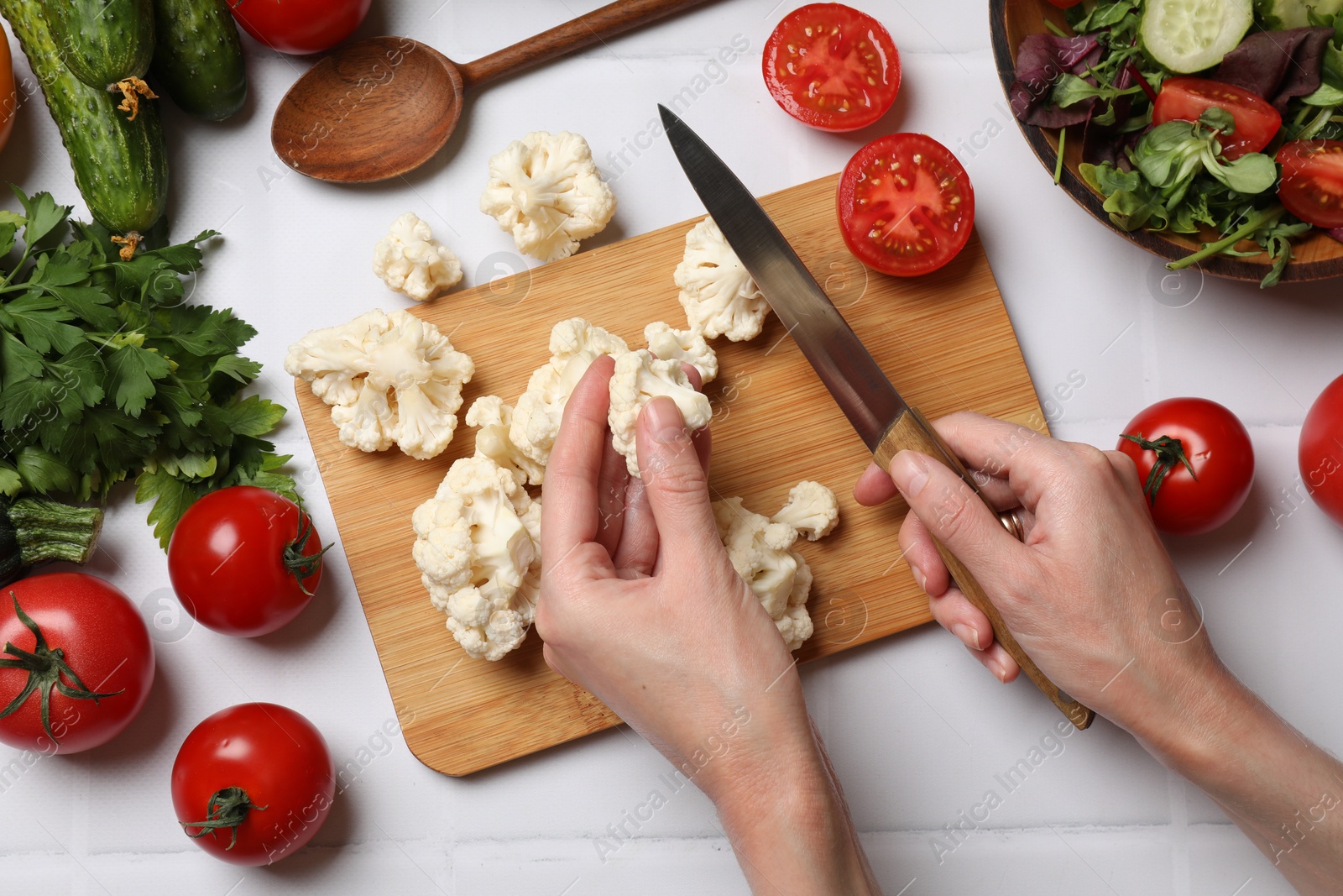 Photo of Healthy vegetarian food. Woman cutting cauliflower at white tiled table with vegetables, top view