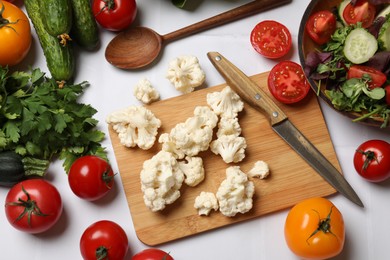 Photo of Healthy vegetarian food. Pieces of cauliflower, salad and vegetables on white tiled table, flat lay